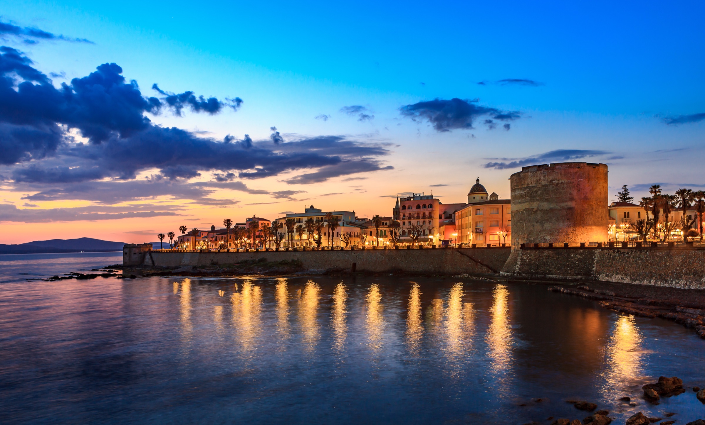 Alghero seafront at sunset, with the old town towers reflected in the bay