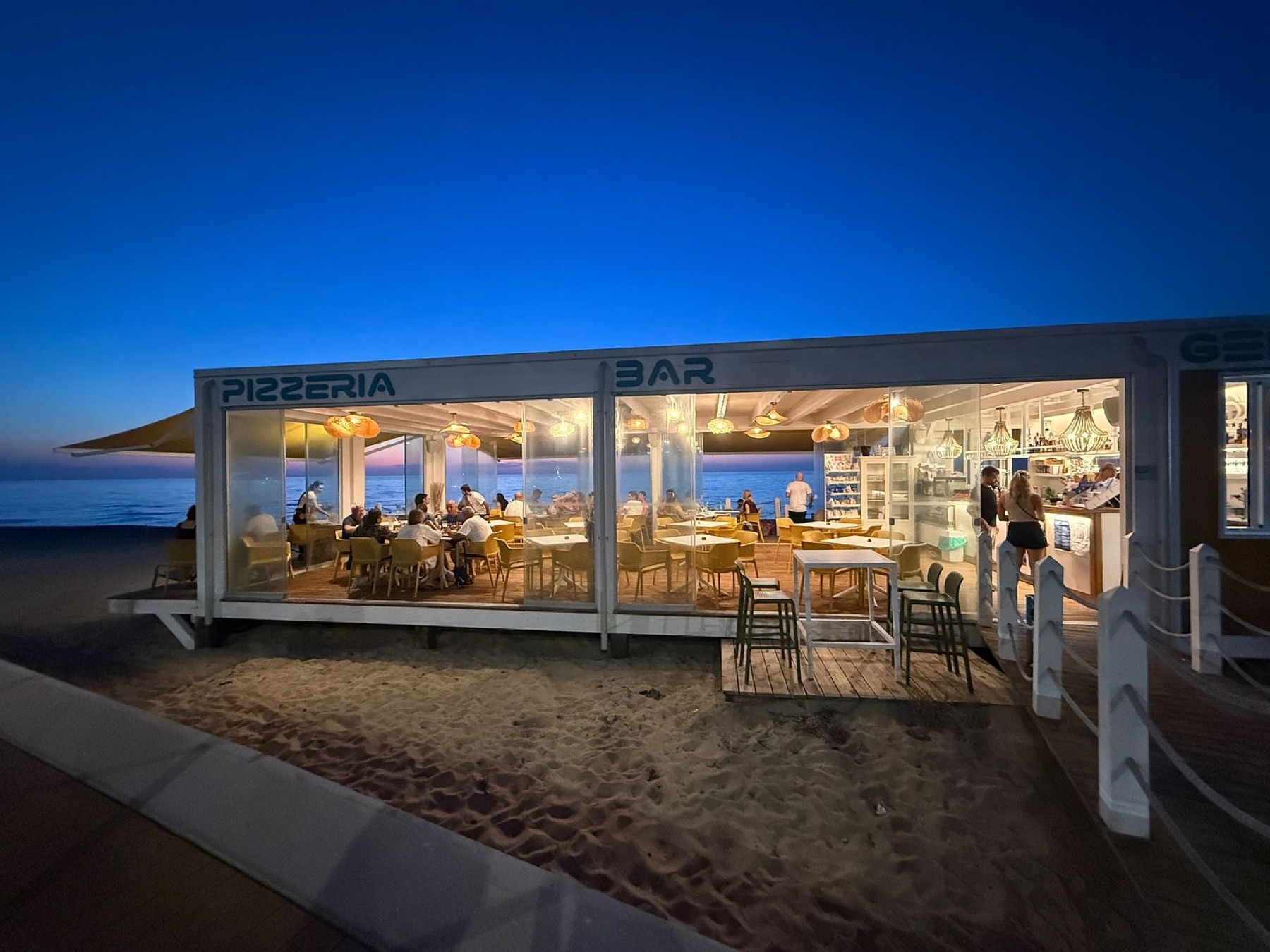 Emerald Beach Club's glass-walled pizzeria and bar at blue hour, directly on Li Junchi beach
