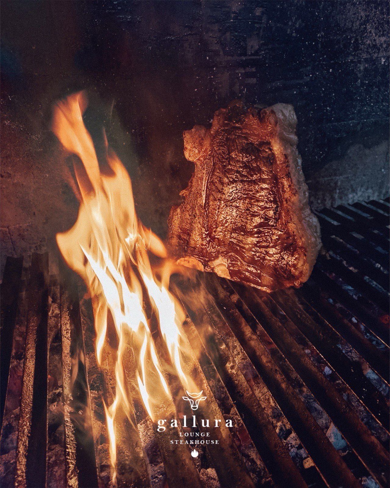 A thick cut of beef on the grill with flames at Gallura Lounge Steakhouse